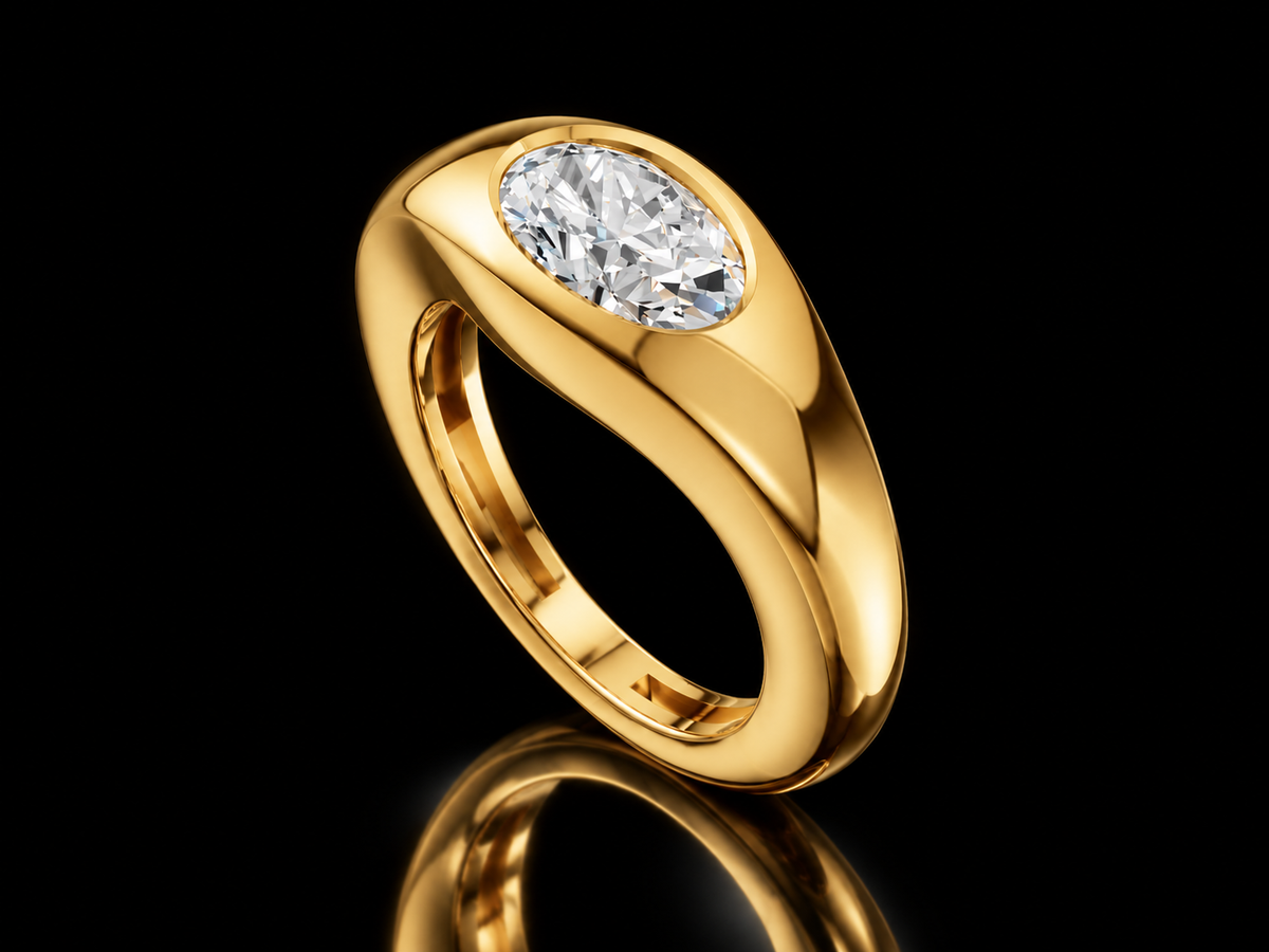East-West oval diamond signet ring in yellow gold standing on black floor with reflection